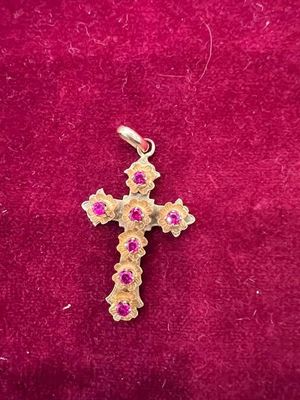 une croix en or sertie de pierres roses, posée sur un fond de velours rouge