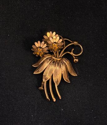 une photo d'une broche ornée de fleurs, posée sur un tissu noir