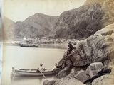 an old photo of a man sitting on a rock next to a boat