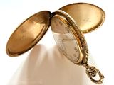 une montre de poche en or posée sur une surface blanche