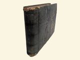 an old book with a black cover sitting on top of a white surface