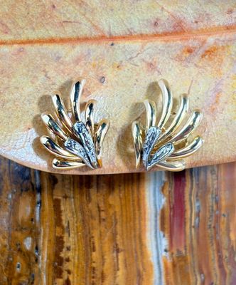 a pair of gold earrings sitting on top of a wooden table
