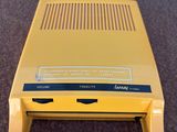 une vieille console Nintendo jaune posée sur un sol recouvert de moquette