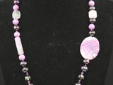 un collier composé de perles violettes et d'un disque blanc, présenté sur un mannequin noir