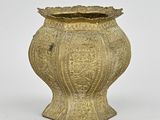 un vieux vase doré posé sur une surface blanche