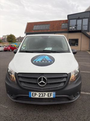 une camionnette blanche garée sur un parking, avec un immeuble en arrière-plan