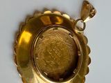 a gold pendant with a coin in it on a white surface