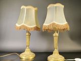 pair of gold table lamps with fringed lampshads on a black table