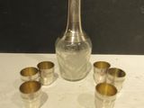 une bouteille en verre et quatre verres à shot posés sur une table