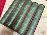 six green books on a table with a red bag