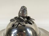 a silver plate with a silver lid and a bird on it