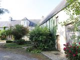 a driveway leading to a stone building with a red rose bush in front of it