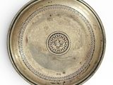 une assiette ancienne en argent sur fond blanc, ornée d'un motif décoratif