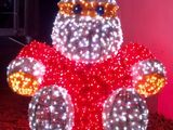 un Père Noël illuminé, assis sur un rocher devant un mur rose
