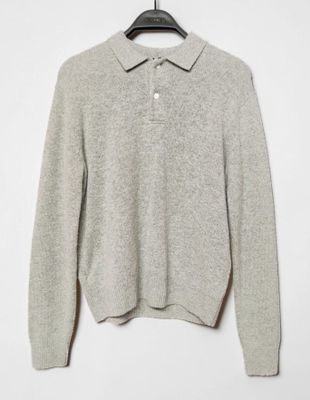 un pull gris suspendu à un cintre sur un mur blanc