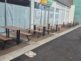 Des tables et des bancs sont alignés sur le trottoir devant un magasin.