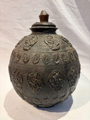 un grand vase en métal muni d'un couvercle, posé sur une surface blanche