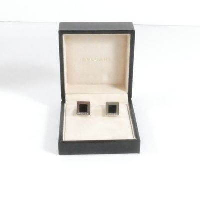 une paire de boutons de manchette noirs et blancs, présentés dans un coffret noir posé sur un fond blanc