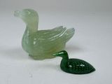 un canard en verre vert posé à côté d'une feuille verte