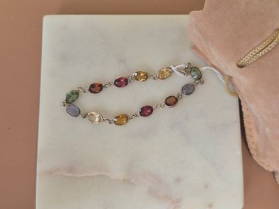 bracelet with multi colored stones on a marble surface with a pink velvet bag