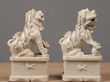 pair of white porcelain foo foo foo statues on a wooden table