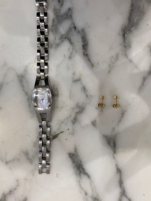 une montre posée sur un plan de travail en marbre, à côté d'une paire de boucles d'oreilles