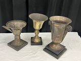 trois vases en argent posés les uns à côté des autres sur une table