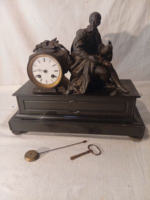 une statue représentant un homme assis sur une table, à côté d'une horloge