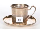 une tasse et une soucoupe anciennes en argent, posées sur une soucoupe portant le chiffre 12
