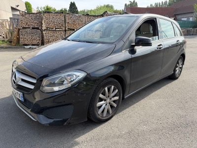 the mercedes b - class is parked in a parking lot in front of a pile of logs