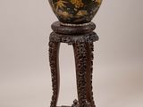 une image représentant un vase noir et doré posé sur un socle en bois