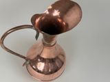 a small copper pitcher with a handle on a table