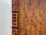 an old brown book with gold trim sitting on top of a white table