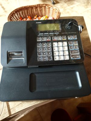 a cash register sitting on a table with a basket of fruit in the background