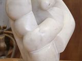 une sculpture en marbre représentant un poing, posée sur un socle transparent