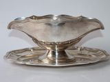 une assiette en argent posée sur une soucoupe, le tout sur une surface blanche