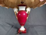 a red and white vase on a table with a gold lamp shade