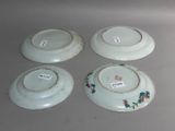 four white plates with floral designs on them sitting on a table