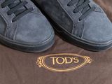 todd ' s grey sued sneakers with black laces on top of a brown box