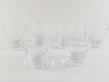 six clear glasses are lined up on a white surface