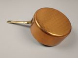 a small copper pot with a handle on a white surface