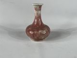 un petit vase rouge posé sur une surface blanche
