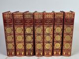 six livres rouges ornés de médaillons dorés sont alignés sur une surface blanche