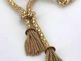 a close up of a gold necklace with a tassel on it