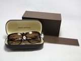 des lunettes de soleil dans un étui, posées sur une surface blanche, avec une boîte marron