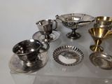 a lot of silver dishes and cups on a glass table