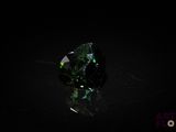un gros plan d'un diamant vert posé sur une surface noire