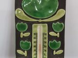 a green frog that is sitting on a thermometer