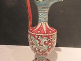 a red and blue vase with a gold handle on a white table