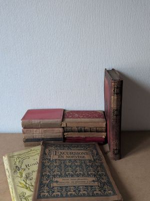 Plusieurs vieux livres sont empilés sur une table, avec un mur blanc en arrière-plan.